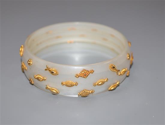 A yellow metal mounted mother of pearl bangle, decorated with geometric shapes.